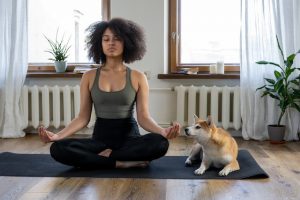 A woman meditating next to her dog.